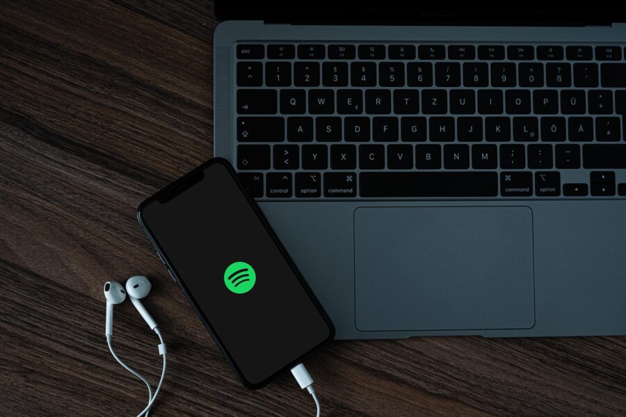 Ein Teil eines Laptops, darauf liegend ein Handy, dass gerade Spotify startet auf einem Tisch stehend.