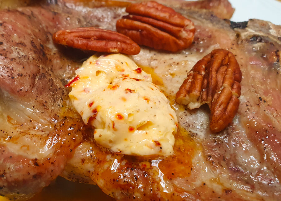 Auf einem weißen Teller im Ofen gegarter Schweinenacken mit schmelzender Knoblauch-Chili-Butter und garniert mit Pekannüssen.
